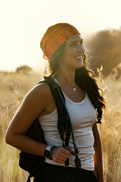 Woman with a backpack and orange headscarf standing in a field